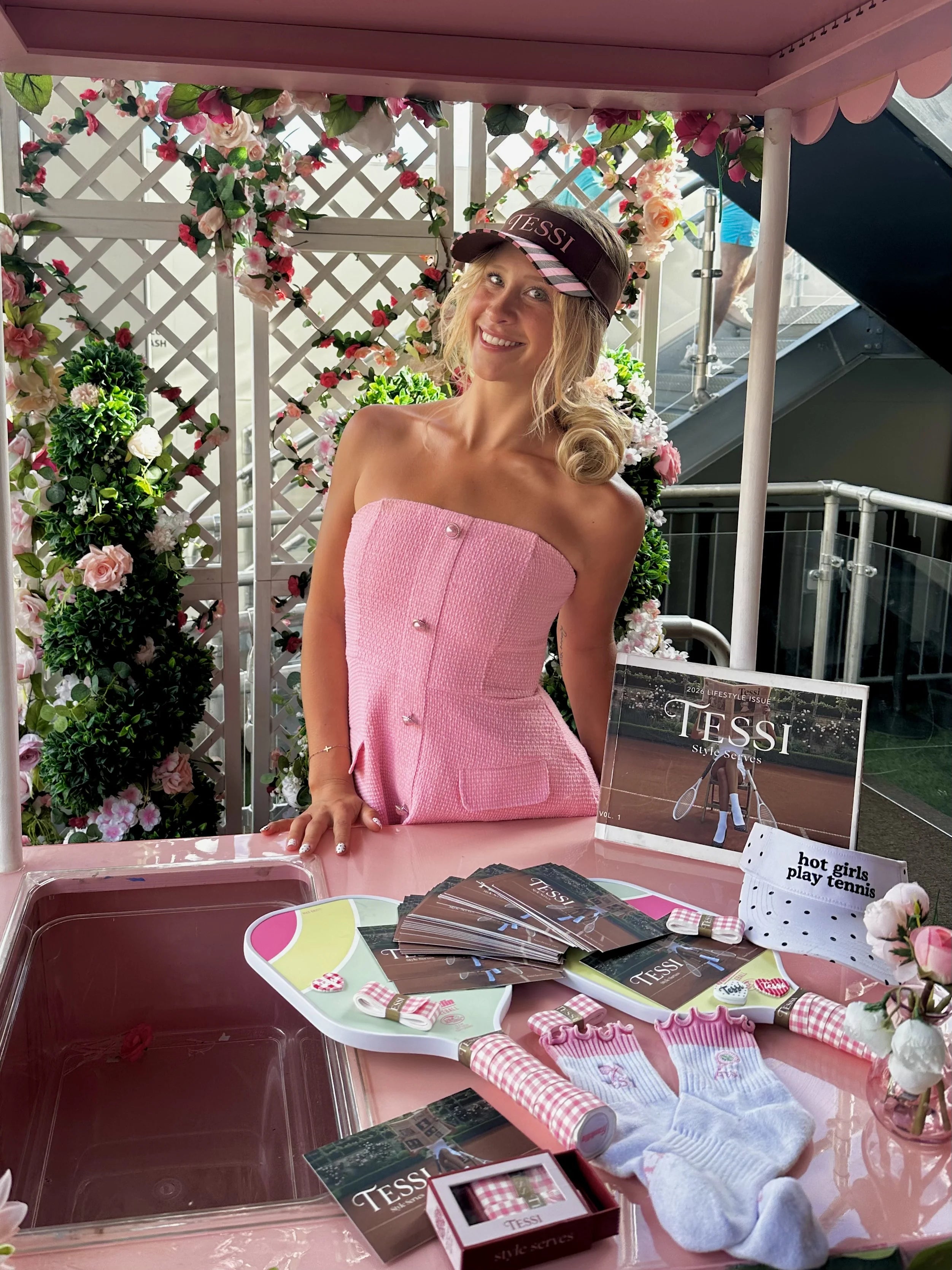 Liv at the TESSI pop-up stand with pink visor, TESSI newspaper, socks, and branded merchandise